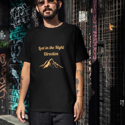 Person wearing a black t-shirt with gold text and mountain graphic against a graffiti-covered wall.
