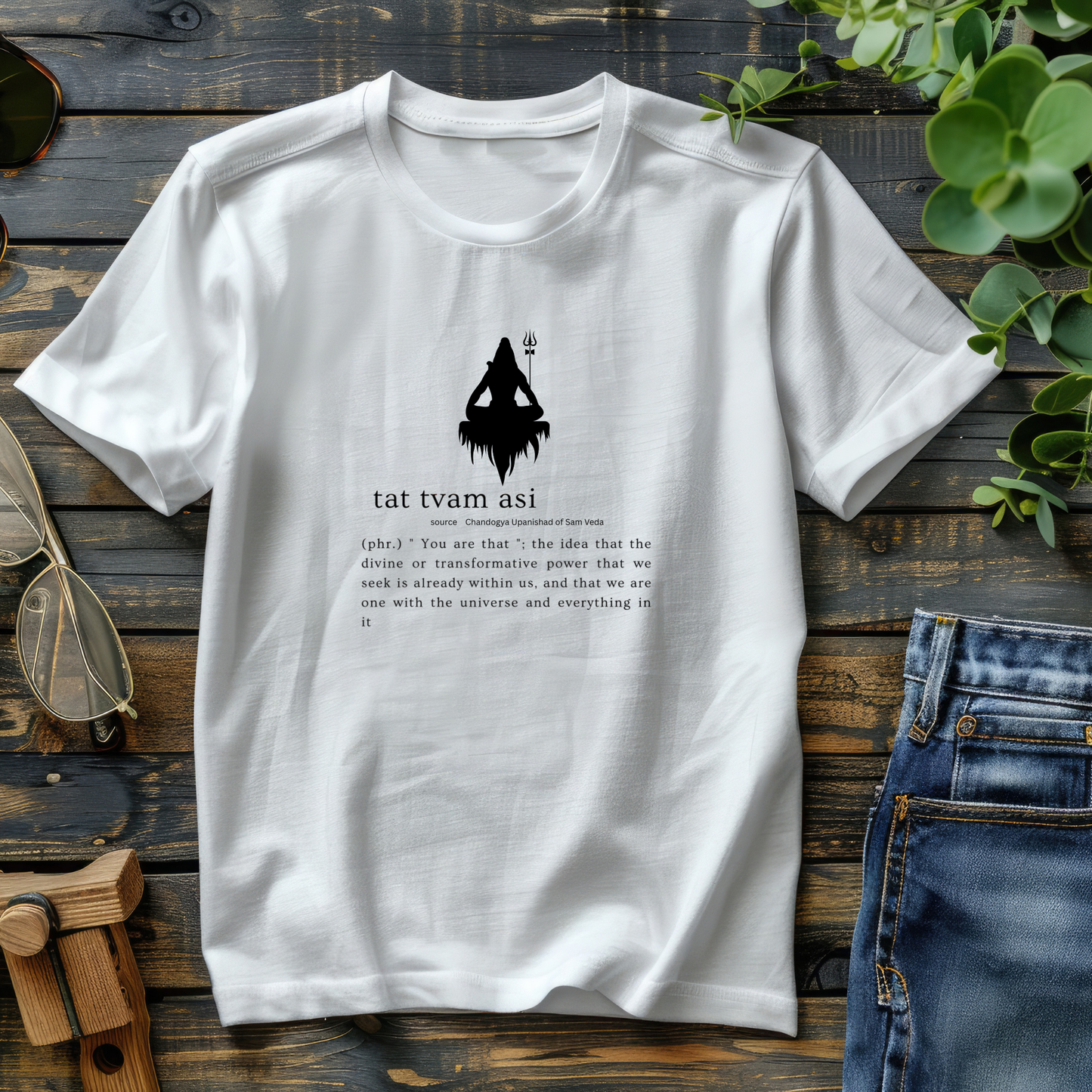 White t-shirt with black graphic and text on a wooden surface with jeans and sunglasses.