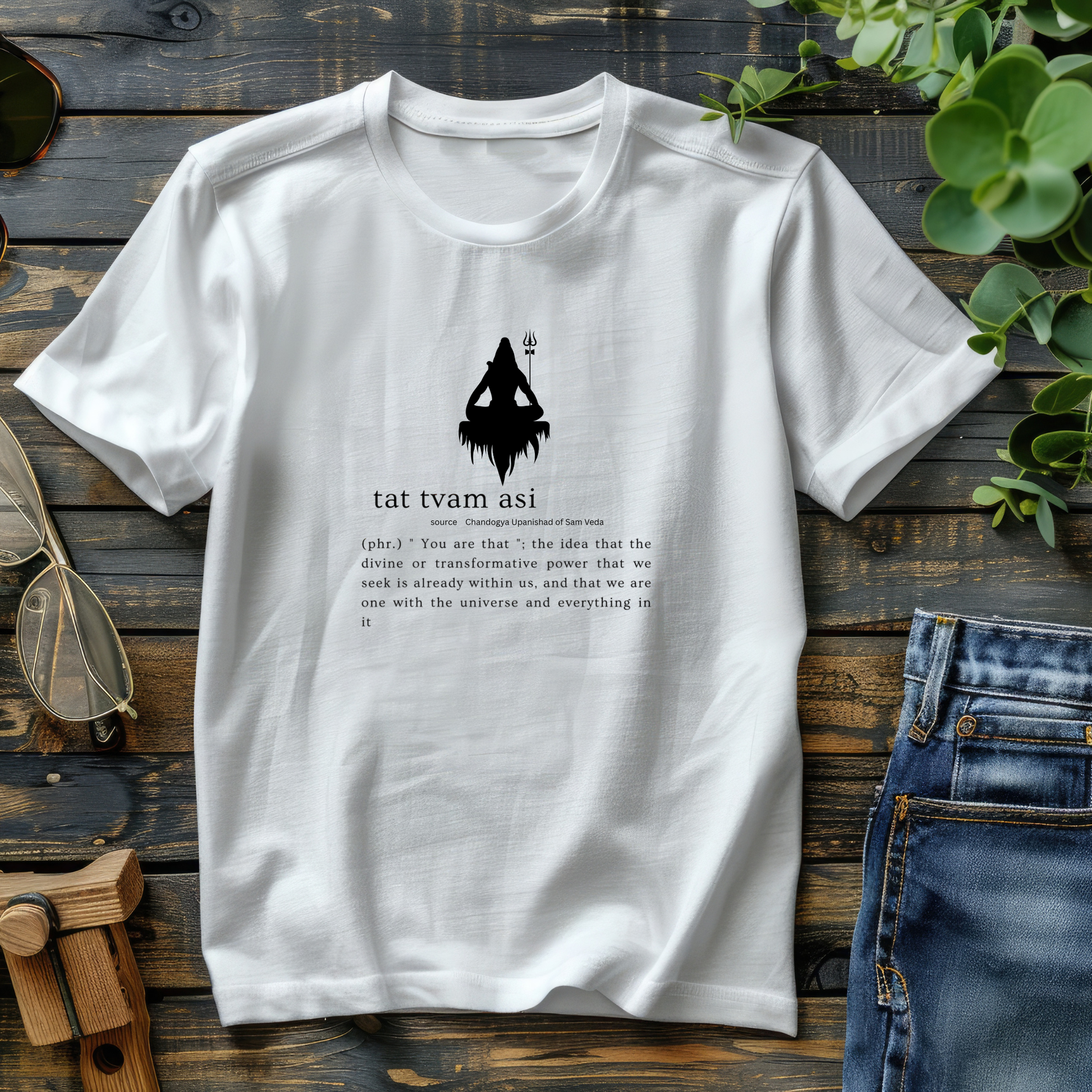 White t-shirt with black graphic and text on a wooden surface with jeans and sunglasses.