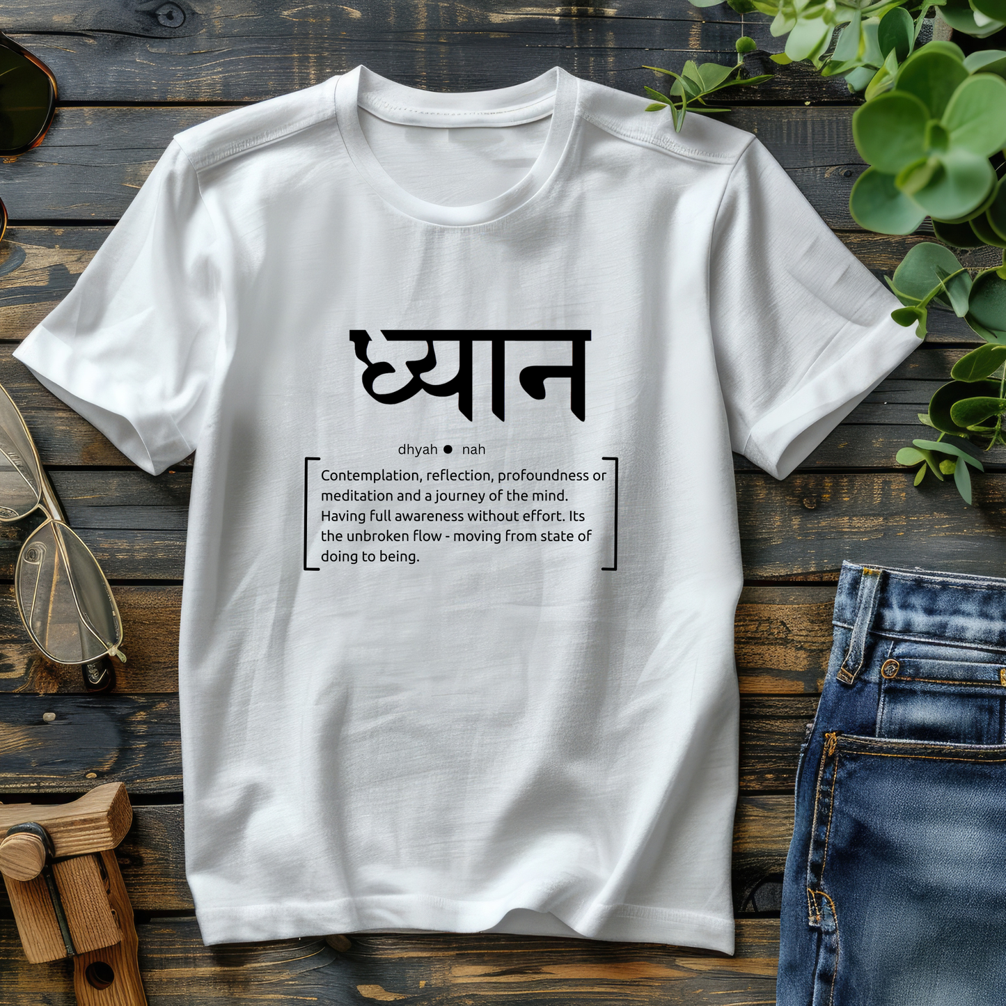 White t-shirt with black text on a wooden surface with jeans and sunglasses.