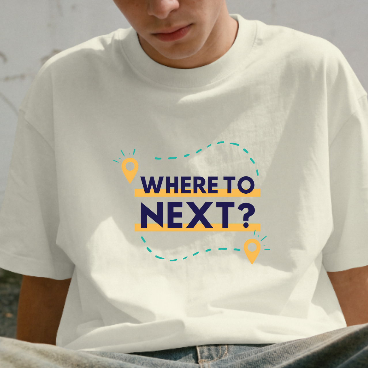 Person wearing a white t-shirt with 'WHERE TO NEXT?' text sitting against a wall with graffiti.