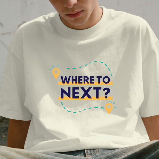 Person wearing a white t-shirt with 'WHERE TO NEXT?' text sitting against a wall with graffiti.