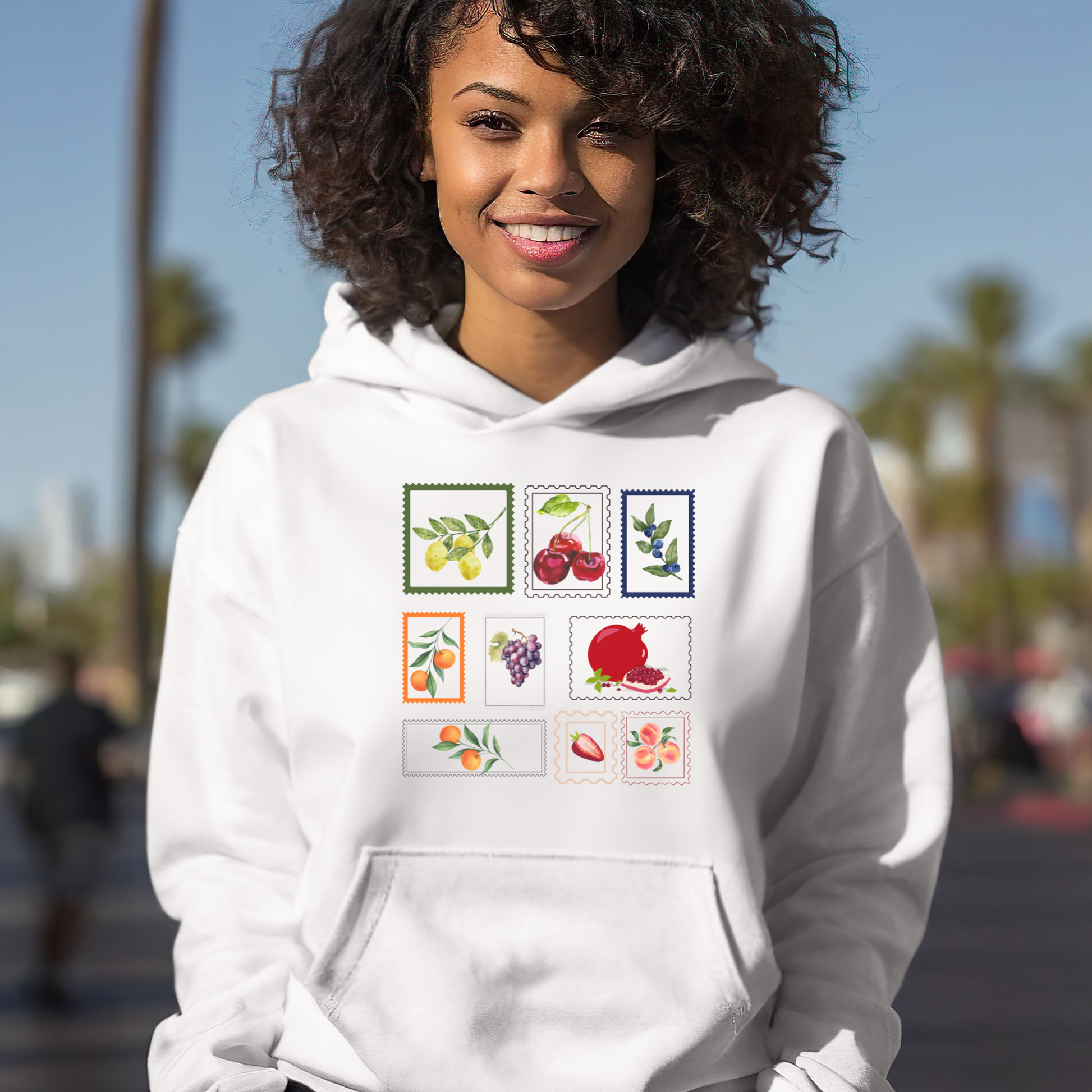 Woman wearing a white hoodie with fruit illustrations on a blurred street background